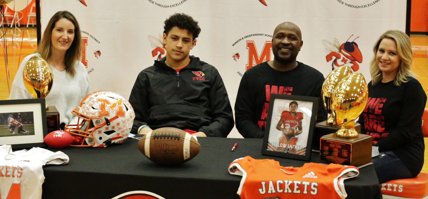 Flanked by his mother Andrea McCoy (left) and his father and stepmother Mark and Micah Kendrick, Yellowjacket senior Kobe Kendrick signs his acceptance of a scholarship to play football at Trinity Valley Community College.